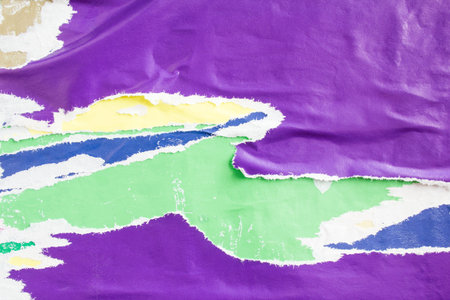 Green and purple torn ripped and crumpled paper placards on billboard with old peeling posters...