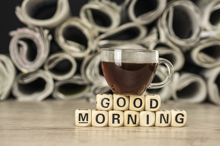 Close up shot of a glass cup of coffee and newspaper. Good morning phrase assembled with wooden letter blocksの写真素材