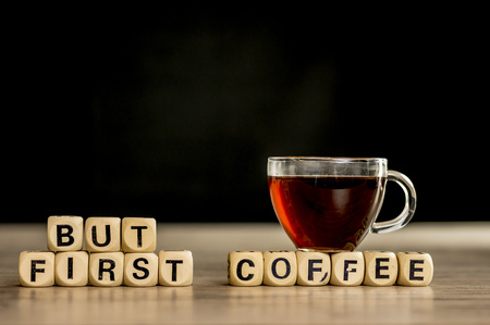 Glass cup of coffee sitting on wooden letter blocks that assemble the phrase but first coffeeの写真素材