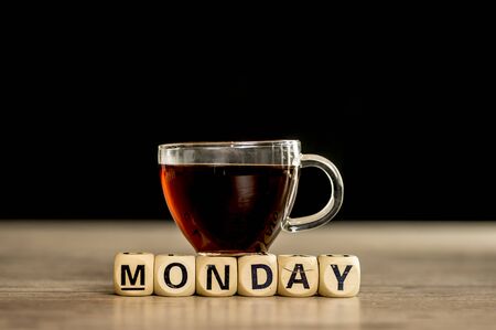 Glass cup of coffee sitting on wooden letter blocks that assemble the word Mondayの写真素材