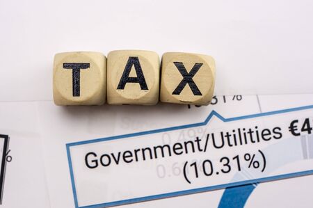 Wooden letter blocks assemble the word tax on a sheet with government tax analysisの写真素材
