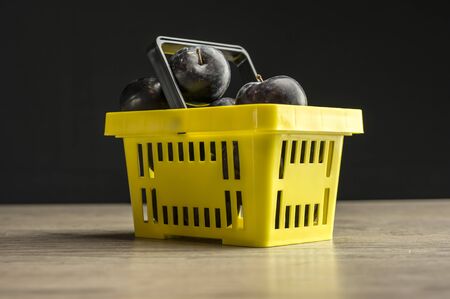 Close up shot of a yellow supermarket basket filled with plumsの写真素材
