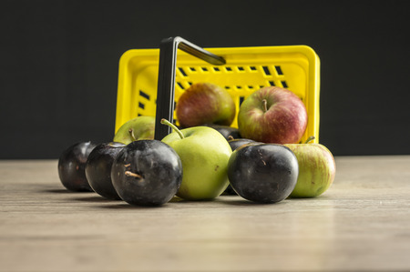 Close up shot of a yellow supermarket basket filled with plums and applesの写真素材