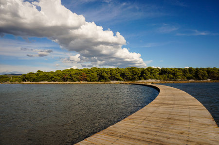 curved wooden boardwalk is connecting the mainland with an island clouds are mirroring the shape of this boardwalkの写真素材