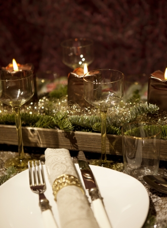 christmas place setting with candles, are wine glasses on the table, pine tree branches are adorned with decorative snowの写真素材