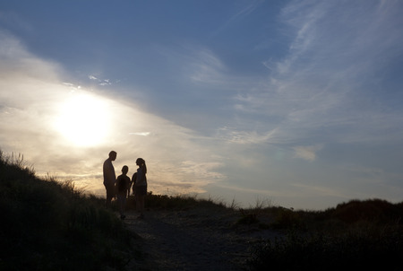 Family standing on a dune in Denmark and watched the sunsetの写真素材