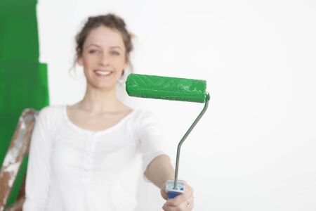 a woman painting a wall green and holds the paint roller to the cameraの写真素材