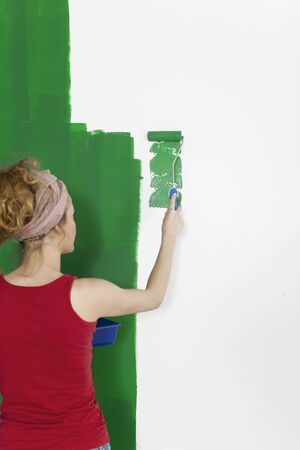 a woman painting a wall green and holds the paint roller to the cameraの写真素材