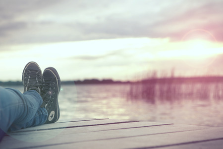 a woman relaxing on a jetty by the lake at duskの写真素材