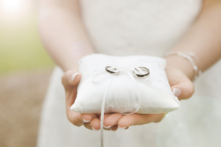 A bride holds a ring pillow with the new wedding rings in her handsの写真素材