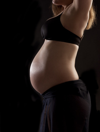 Pregnant woman with baby belly in front of black backgroundの写真素材
