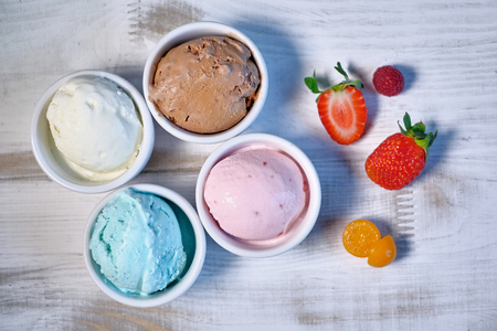 Selection of gourmet flavours of Italian ice cream in vibrant colors served in individual porcelain cups on an old rustic wooden table in an ice cream parlor, angle view jpgの写真素材