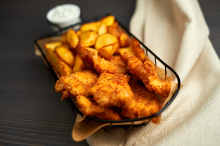 Nuggets and baked potatoes in a beautiful basket with white sauceの写真素材
