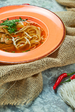Noodle and beef soup on a light gray textured background. Beautiful serving dishes. Restaurant menu