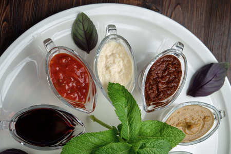 colored sauces in bowls on a white round plate on a dark wooden background.