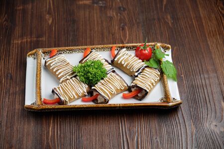 Eggplant rolls with greens on a white plate on a dark wooden background.の写真素材