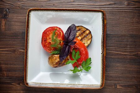 Grilled vegetables on a white plate on a dark wooden background.の写真素材
