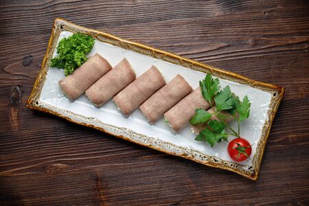 ham rolls with filling decorated with greens on a rectangular white plate on a dark wooden background.の写真素材