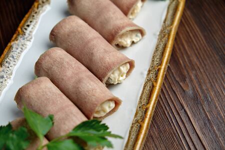 ham rolls with filling decorated with greens on a rectangular white plate on a dark wooden background.の写真素材