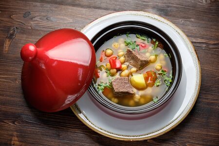 Beef soup in a pot with a red lid on a dark wooden background. Restaurant menuの写真素材