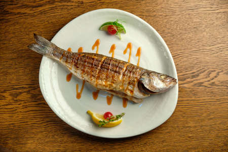 Grilled seabass fish with sauce and lemon on wooden backgroundの写真素材