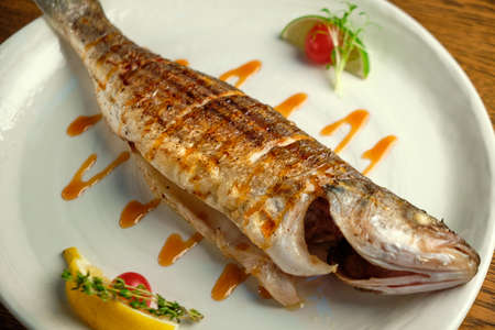 Grilled fish with sauce and lemon on wooden table, closeupの写真素材