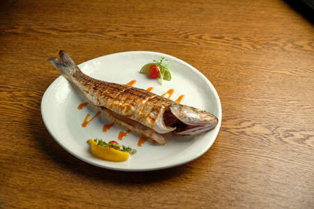 Fried fish on a white plate on a wooden table. Restaurantの写真素材