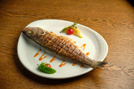 Grilled fish with tomato sauce on white plate on wooden table.の写真素材