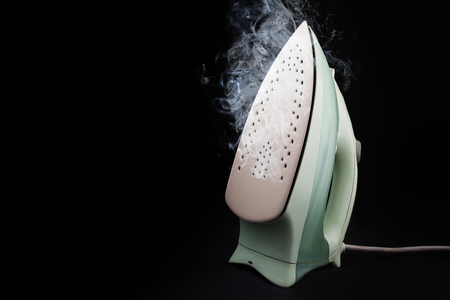 A light iron with steam clubs on a black background with a place for an inscription.の写真素材