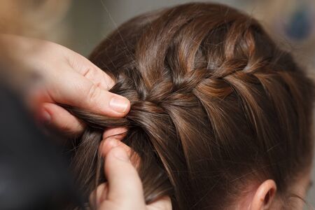 Female hands braid dark hair, close-up.の写真素材