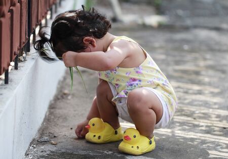 little girl playing outdoor and sitting on groundの写真素材