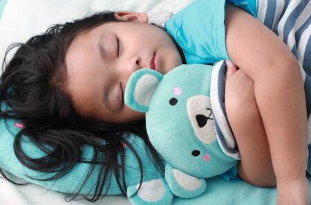 closeup shot of cute little asian girl sleep and hug teddy bearの写真素材