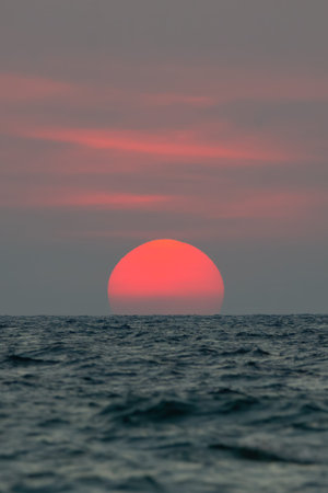 The sun fell to the sea, the bottom of the sun was blocked by the horizon. The sky is orange and the sea is dark.