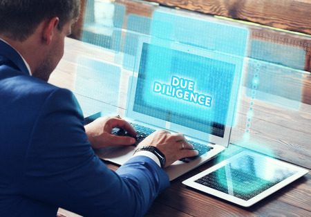 Business, technology, internet and networking concept. Young businessman working on his laptop in the office, select the icon Due diligence on the virtual display.の写真素材