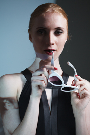 Young beautiful girl with glasses in hands posing in studio.の写真素材