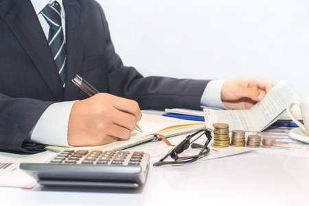 Male manager putting his ideas and writing business plan at workplace,man holding pens and Bank money book, making notes in documents, on the table in office concept for property, mortgage and invest.の写真素材