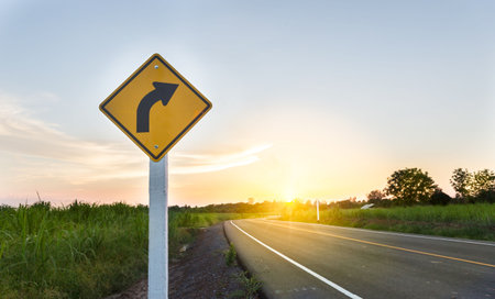 Countryside road ,Sign curved road on the way at the natural Sunset Sunrise Over Field Or Meadow. Countryside Landscape Under Scenic Colorful Sky At Sunset Dawn Sunrise. Warm Colours.の写真素材