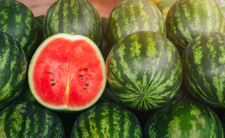 Several large sweet green watermelons and cut watermelons, several large sweet green watermelons are placed on a wooden table on a natural background for sale.の写真素材