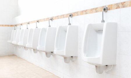 Men's room with white porcelain urinals in line. Modern clean public toilets with tiles . Comfort male toilet urinal concept.の写真素材