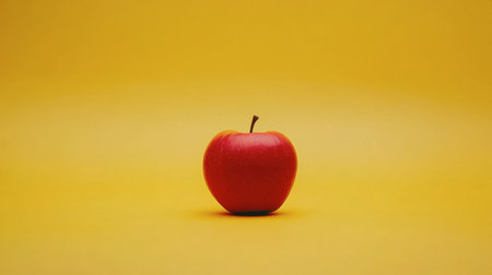 A single bright red apple placed on a vivid yellow background, creating a bold contrast.の素材
