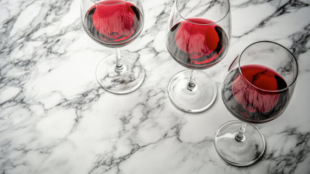 Three elegant red wine glasses filled with rich wine sit on a smooth marble surface, perfect for dining settings, celebrations, or intimate gatherings.の素材