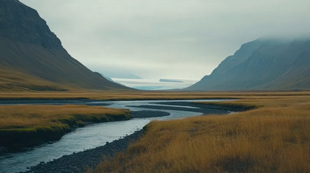 A breathtaking view of a winding river flowing through a serene valley, surrounded by misty mountains and golden grass, creating a peaceful natural landscape.の素材