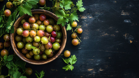 A bowl of Indian gooseberries surrounded by their leaves and a few scattered fruits, set on a dark wooden surface to highlight their vibrant color and natural appeal.の素材