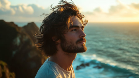 A man with medium-length wavy hair standing on a cliff, his hair blowing in the strong ocean breeze.の素材