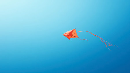 A red kite flying high in the sky, with its tail fluttering in the wind against a bright blue background.の素材