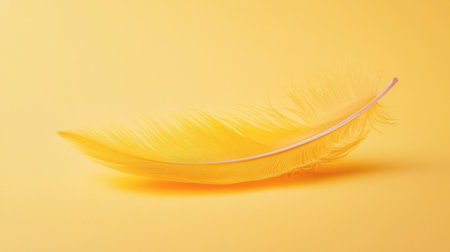 A single yellow feather floating gently against a soft yellow background.の素材