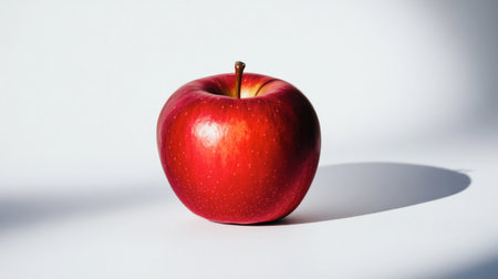 A vibrant red apple placed on a white background, creating a simple yet striking contrast that draws attention to the fruit.の素材