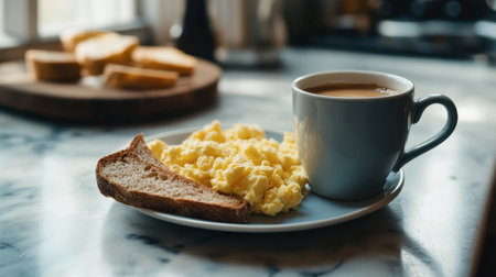 A coffee cup on a marble countertop next to toasted rye bread and scrambled eggs.の素材