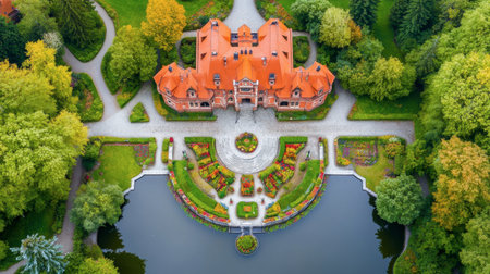 Captivating aerial view showcasing an elegant mansion surrounded by vibrant gardens and lush trees, with a serene pond reflecting its beauty.の素材
