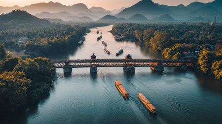A stunning aerial view of the River Kwai Bridge, with boats traveling underneath and mountains in the distance.の素材